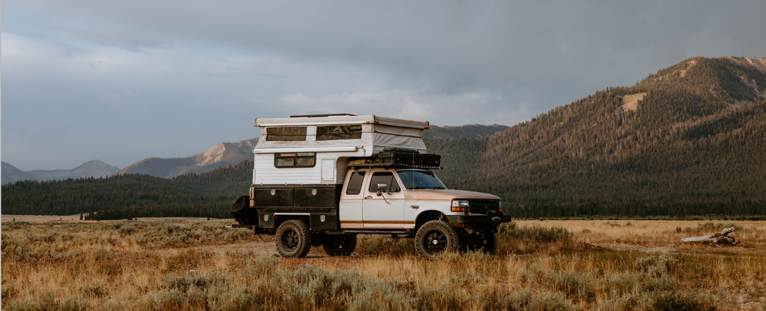Truck camper setup in a scenic mountain location, showcasing overlanding gear and off-road vehicle amidst the mountains.