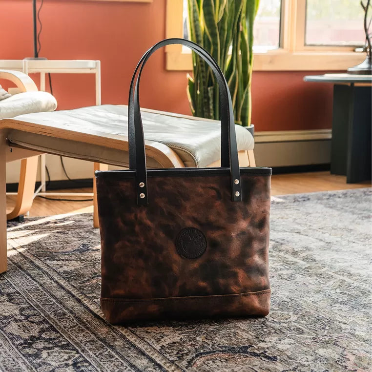 Brown leather tote bag on a patterned rug with a blurred indoor background