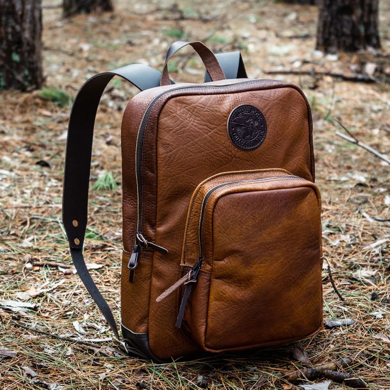Brown leather backpack on a forest floor